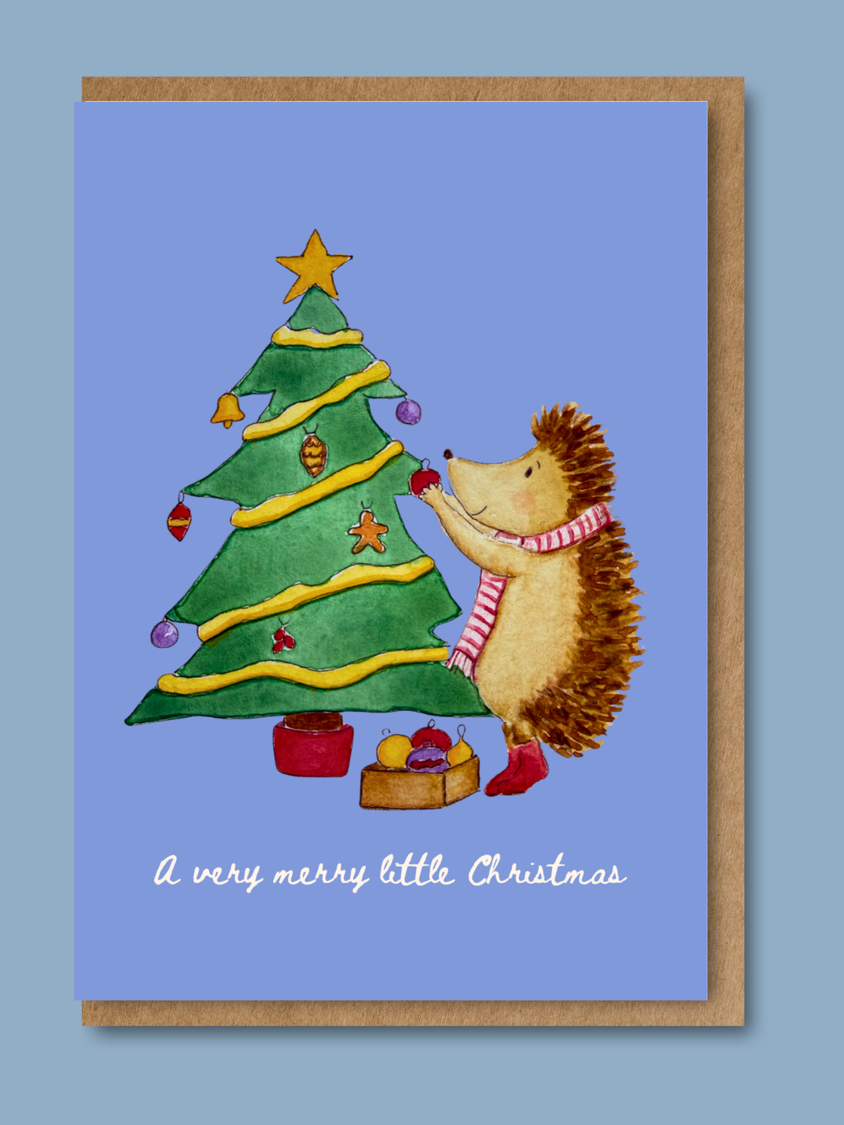Blue Christmas card with hand-illustrated watercolour hedgehog decorating a Christmas tree